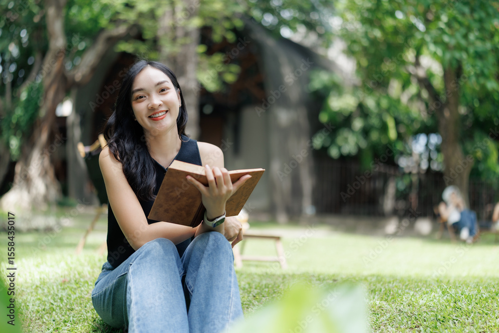 Fototapeta premium Young woman reading a book in a peaceful garden setting