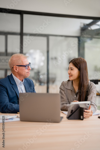 Wallpaper Mural Senior businessman and young businesswoman engaging in a discussion during a business meeting, utilizing a laptop and tablet in a modern office environment, fostering collaboration and teamwork Torontodigital.ca