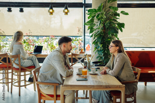 Foto Young couple talking seriously at cafe table, woman working on laptop in backgro