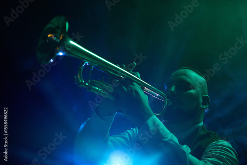 Photography A musician plays the trumpet on a dimly lit stage with blue and green spotlights and atmospheric smoke