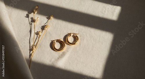 Gold hoop earrings with dried flowers resting on beige fabric in soft sunlight