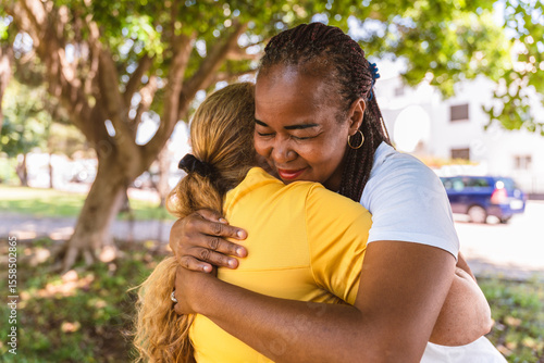 Photos Multiracial friends hugging tightly, sharing genuine bond while standing in sunl
