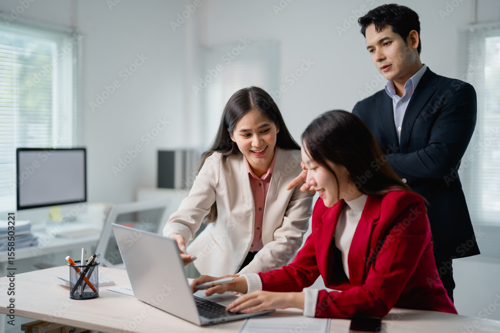 Three smiling Asian businesspeople collaborating on a project while working together at a laptop in a bright, modern office, showcasing teamwork and effective communication Three smiling Asian businesspeople collaborating on a project while working together at a laptop in a bright, modern office, showcasing teamwork and effective communication