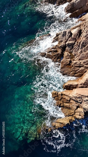 Vue aérienne d’une mer turquoise s’écrasant sur des rochers en Corse, dévoilant la beauté brute du littoral méditerranéen et la transparence de l’eau.