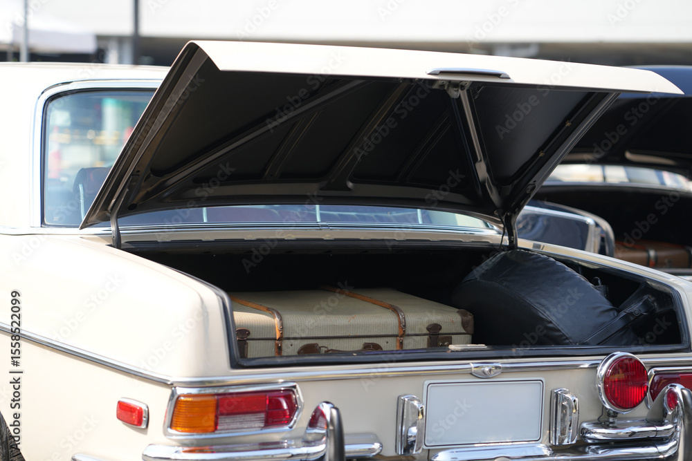 Fototapeta premium A vintage car trunk opened to reveal a vintage suitcase, evoking the sense of travel and elegance. The image highlights the blend of retro automotive design and nostalgic travel elements.
