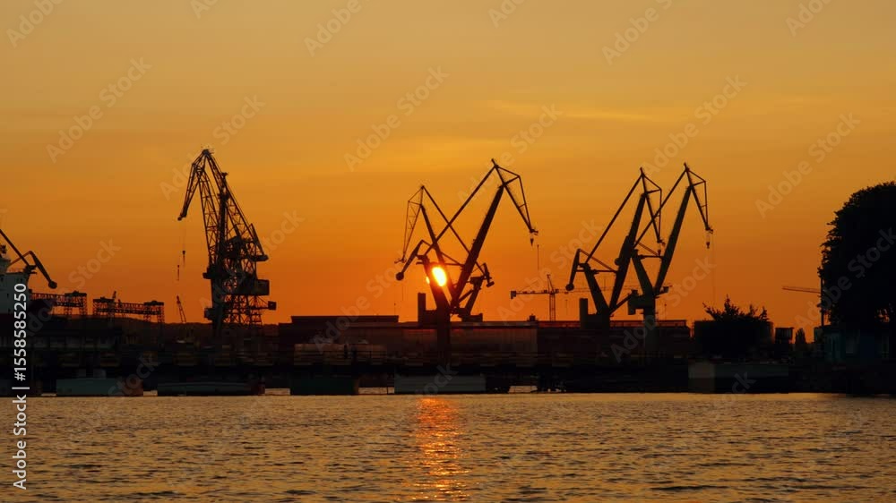 Cranes and boats silhouetted against golden sunset in harbor at dusk Cranes and boats silhouetted against golden sunset in harbor at dusk
