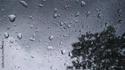 Rainwater running down a car windshield during a rainy day. The blurred background and water droplets create a moody scene. Stormy weather.