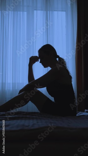 black silhouette upset unhappy woman sitting on bed dark room mood depression sadness emotion. Sad lonely Girl feels bad after party, insomnia migraine suffers headache. window curtains vertical video