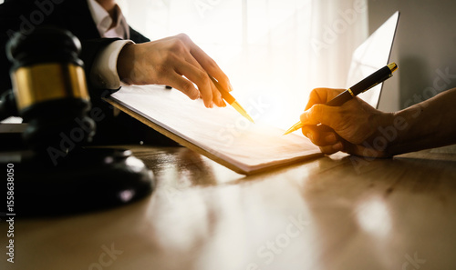 Two hands, one belonging to a legal professional, point to a document for a client to sign, with a gavel and scales of justice nearby.