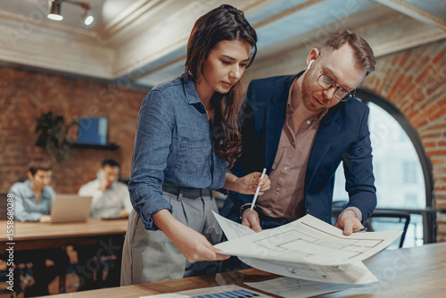 Photos A dedicated professional duo working together on project blueprints within a sty