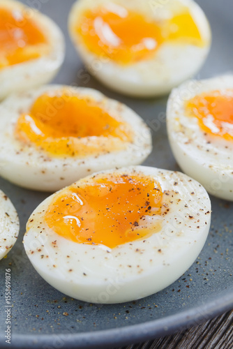 Soft boiled egg halves sprinkled with salt and pepper served on blue plate (Selective Focus, Focus one third into the image)