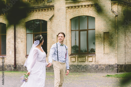 Newlywed couple walking hand in hand in front of an old building, expressing love, joy, and romantic connection, celebrating their wedding day with a calm and tender moment outdoors.
