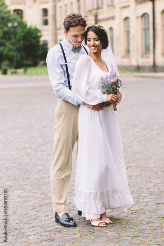 Romantic groom embracing his bride outdoors on their wedding day, expressing love, commitment, and emotional connection in a peaceful, intimate moment captured in soft natural light.