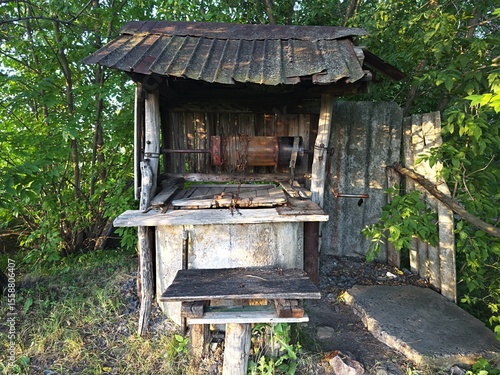 Old rustic water well in a rural village, surrounded by green trees and aged wooden structure. Vintage countryside scene with an abandoned traditional well. Concept of historical architecture and old.