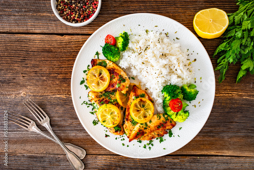 Lemon chicken escalopes with rice on wooden table