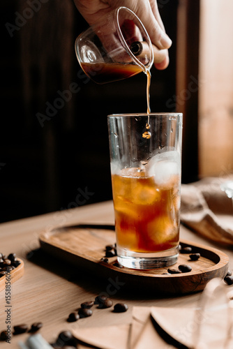 Coffee is being poured into a glass full of ice cubes. Action shot of making a refreshing iced latte.