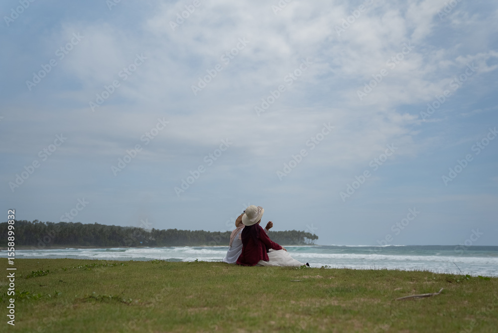 Fototapeta premium Two friends enjoy the beauty of Indonesia's tropical beaches. Two young women sit and talk on a beautiful tropical beach