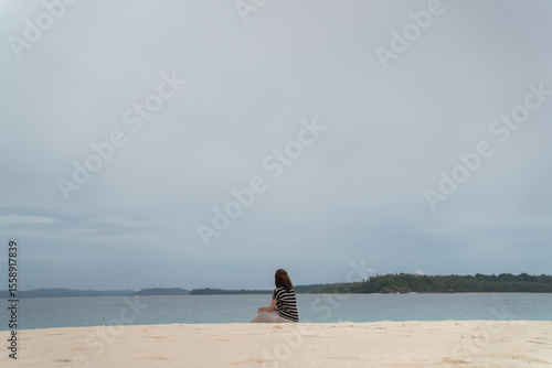A young woman enjoys the beauty of a tropical beach. A young woman sits alone on the beach