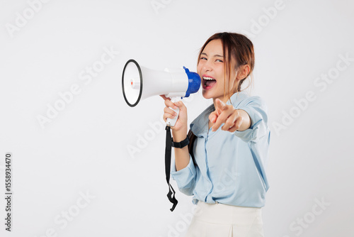 Obraz na plátně A happy young Asian woman points with her finger on camera, shouting into megaphone to announce news