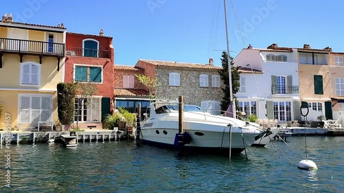 Colorful waterfront houses with balconies and boats docked in a serene harbor of Port Grimaud, showcasing vibrant architecture and a clear blue sky reflecting on the water