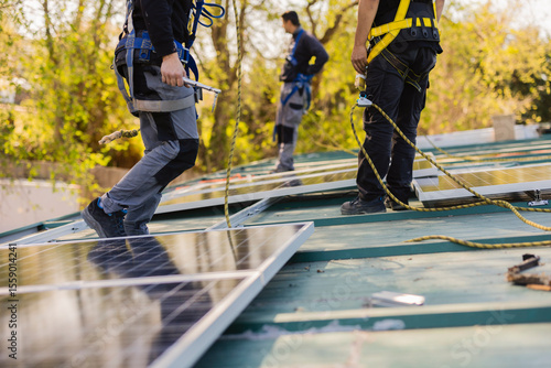 Фотография Workers installing solar panels on rooftop of house using safety harnesses