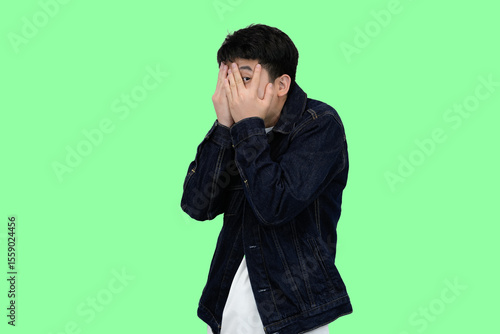 Canvas Print Young Asian Man Covering Face with Hands, Peeking Through Fingers, Green isolate