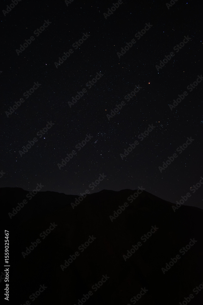 Fototapeta premium 埼玉県秩父市の山の稜線と冬の星空を捉えた風景。澄んだ空に輝くオリオン座が印象的で、静寂な自然美を感じる一枚。星空観察、天体、自然風景、旅行のイメージに最適な写真素材です。