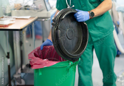 Doctor wearing green scrubs opening biohazard medical waste container in hospital room