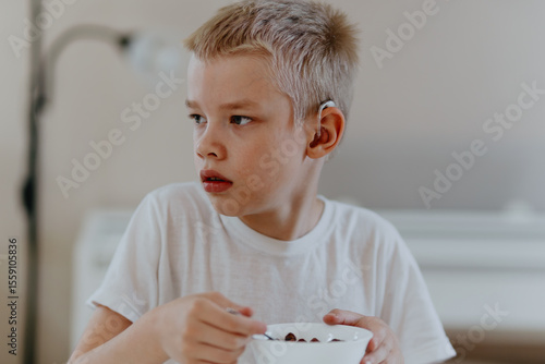A boy with hearing aids enjoys a healthy breakfast, showcasing inclusive daily routines and childhood nutrition. Perfect for disability awareness and parenting content