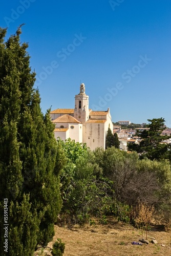 Charming narrow streets of Cadaqués, Spain, with white church on the hill, houses and vibrant blue sky, showcasing the historic Mediterranean coastal town’s beauty and traditional architecture