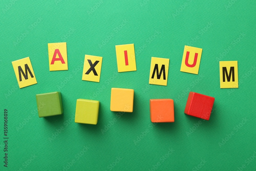 Obraz premium Word Maximum and colorful cubes on green background, flat lay