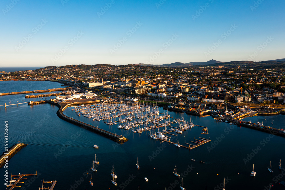 Obraz premium Aerial view of Dun Laoghaire Harbour with sailboats, town, and Dublin mountains during a glowing sunset