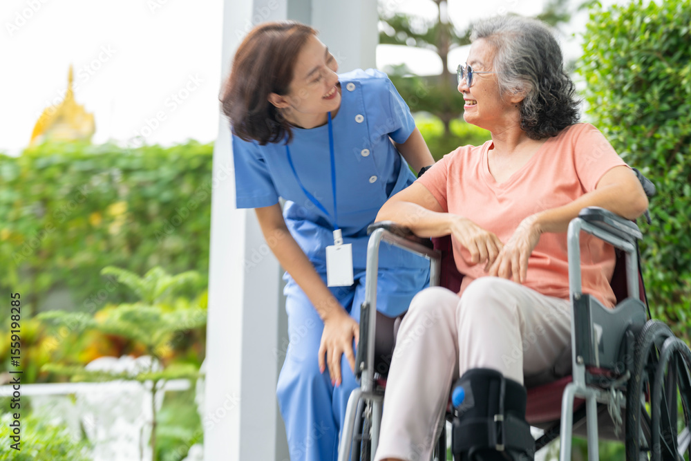 Obraz premium smiling Asian caregiver in scrubs enjoys a moment outdoors with senior woman in a wheelchair, pointing at nature enthusiasm. Concept of home healthcare, assisted living, and positive elderly support.