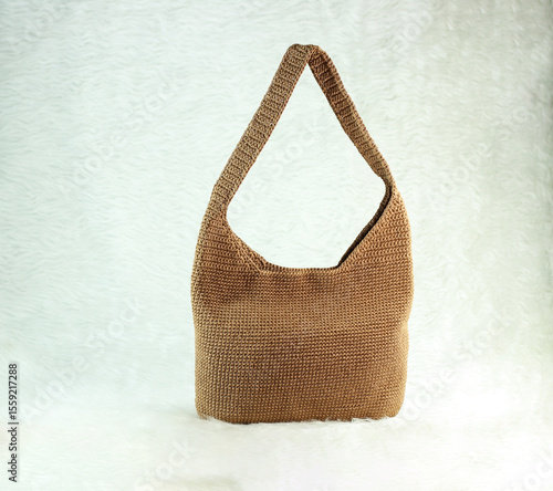 Knitted handmade milky brown bag on furry white blanket. 