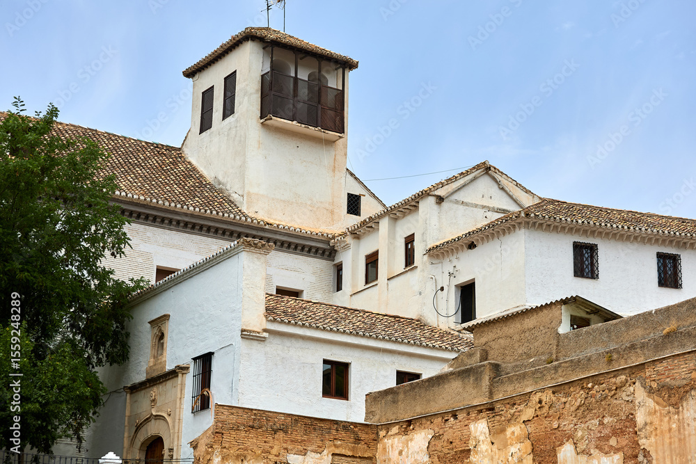 Fototapeta premium Whitewashed Mediterranean building with tiled roofs, small windows, and square tower against blue sky, showing traditional architecture and structure; architecture, facade;
