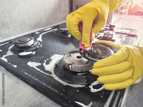 Hands cleaning gas cooker with special white foam in the kitchen