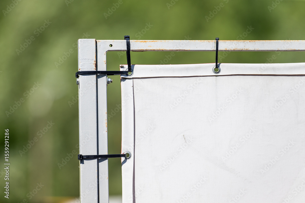 Obraz premium white outdoor banner attached to metal frame with black zip ties closeup advertising sign installation detail on green blurred background for construction commercial marketing 