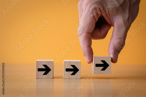 Wallpaper Mural Navigating the Future A Hand Placing a Wooden Block with an Arrow Symbolizing Progress, Direction, and Strategic Planning on a Wooden Surface with Orange Backdrop Torontodigital.ca