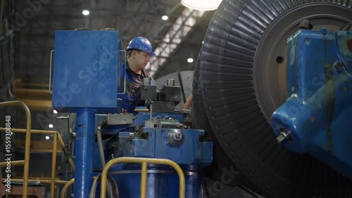 Industrial Mechanic Male Worker In Blue Protection Helmet. Professional Mechanic At An Industrial Metalworking Factory. Industrial Engineer Worker Checks Rotating Mechanical Gas Turbine Engine