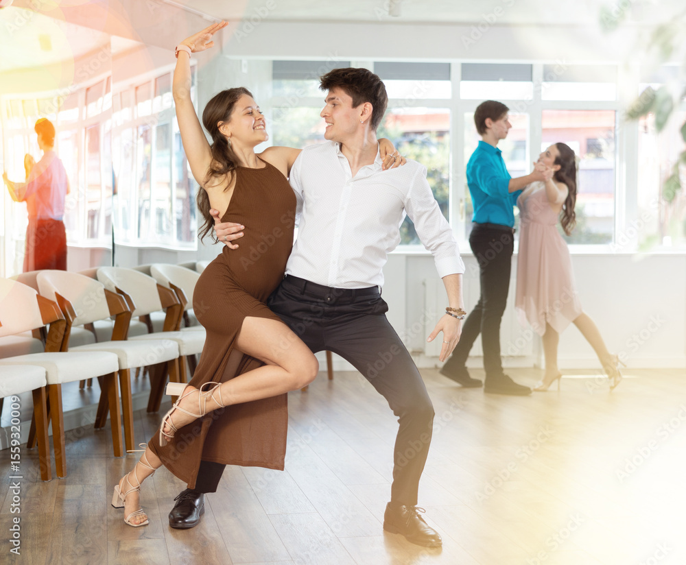 Naklejka premium Positive girl and guy dancing slow ballroom dance during group class in choreography studio