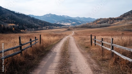 Dirt Road Through A Valley With Wooden Fences And Trees Under A Cloudy Sky