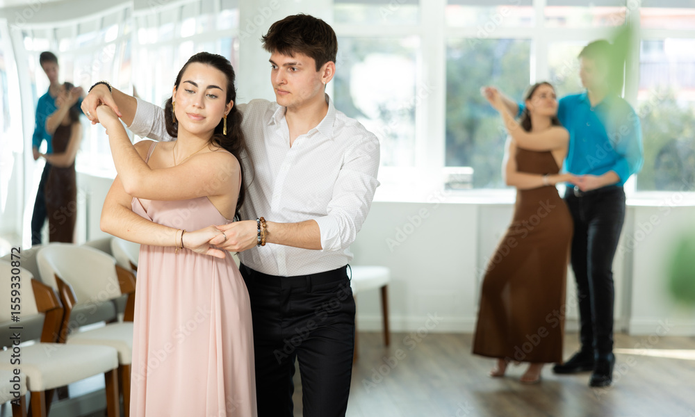 Fototapeta premium While doing rehearsal of reporting concert, guy and girl participants of dance workshop perform quickstep. Two couples practice their skills in performing quickstep during attending dancing school.