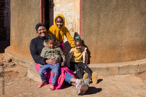 Africa village , african woman mother and children in the yard, in front of round traditional house with thatched roof