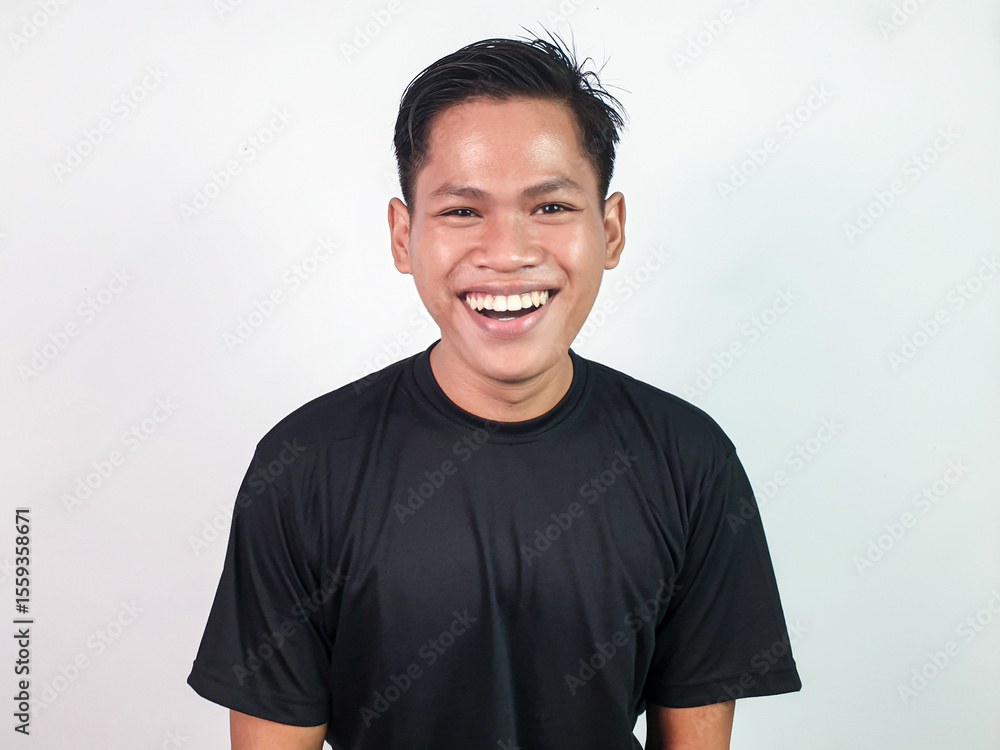 Cheerful Young Man Smiling Brightly Against a White Background. Joyful young man in black shirt displaying genuine laughter, standing in white studio setting, radiating positivity and happiness. Cheerful Young Man Smiling Brightly Against a White Background. Joyful young man in black shirt displaying genuine laughter, standing in white studio setting, radiating positivity and happiness.