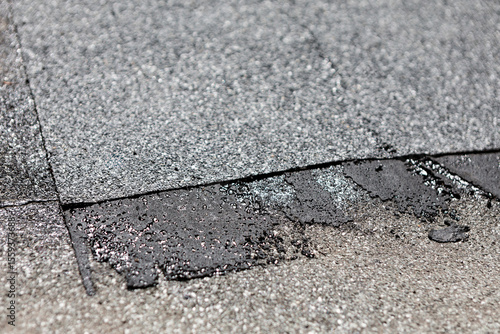 Dark asphalt patch applied to light gray roofing material. Worn patch of roof with visible signs of repair and aging, including rough textures and discolored areas