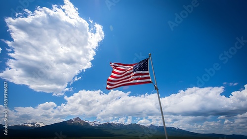 American Flag Waving under a Bright Blue Sky with Clouds and Distant Mountains - Patriotic Outdoor Landscape