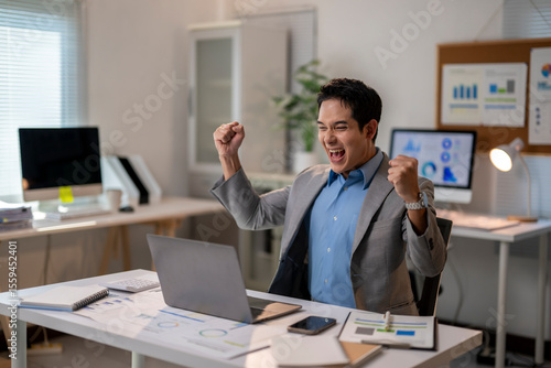 Photos A man is sitting at a desk with a laptop and a cell phone