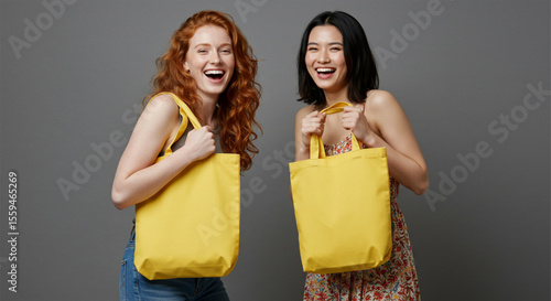Two diverse women holding yellow tote bags studio portrait