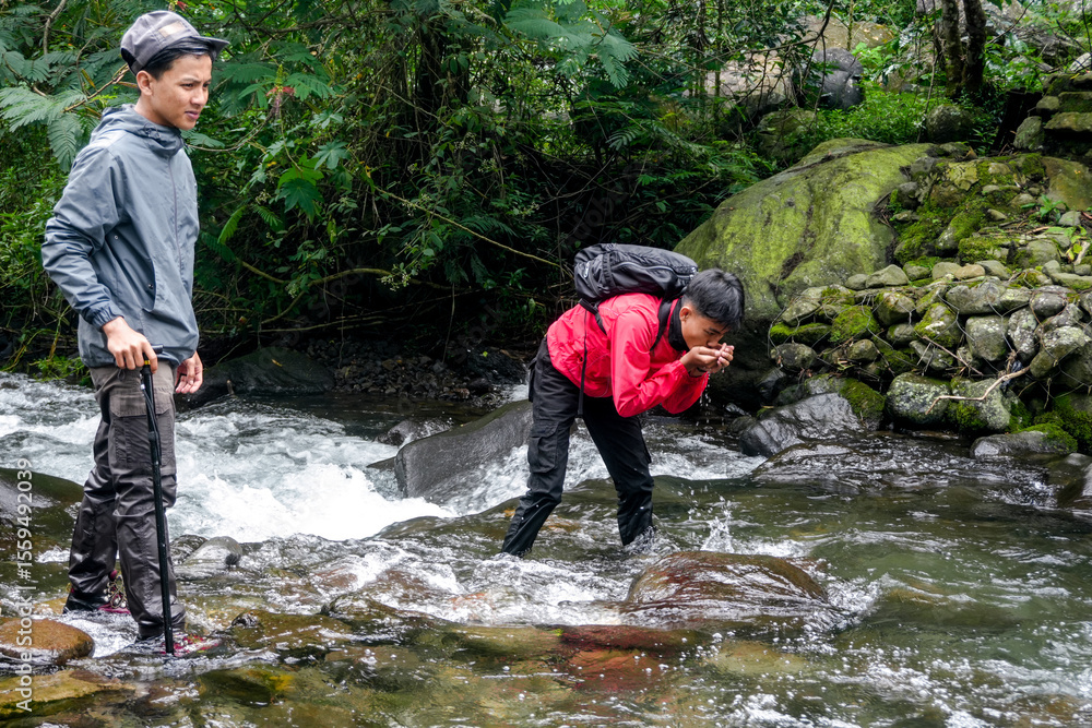 Obraz premium Two Young Trekkers Drinking With River Water