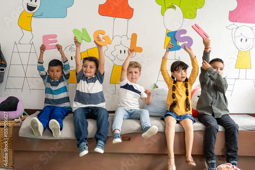Diverse group of preschool children holding large colorful letters spelling “English” in a bright classroom. Early language learning, playful literacy, preschool and kindergarten education